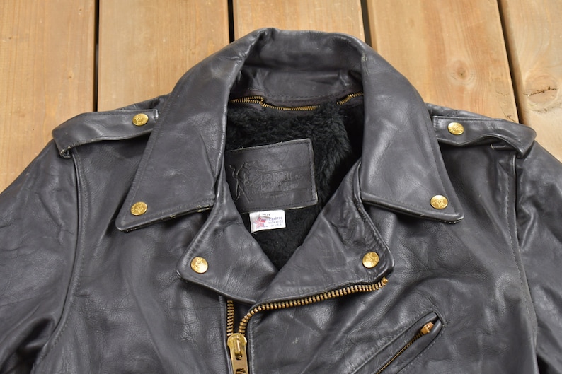 May include: A black leather motorcycle jacket with a zipper closure and gold-toned hardware. The jacket has a fur-lined collar and a label on the inside.
