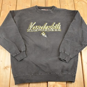 May include: Dark gray crewneck sweatshirt with the text "Vanderbilt Commodores" in yellow and green. The sweatshirt has long sleeves and a ribbed hem and cuffs. A small logo is below the text.