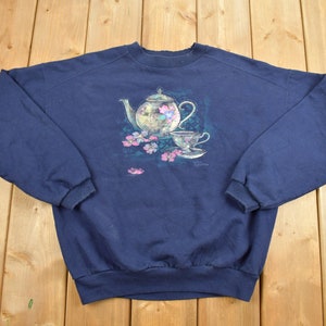 May include: A navy blue sweatshirt with a vintage-style graphic of a teapot and teacup with pink flowers.