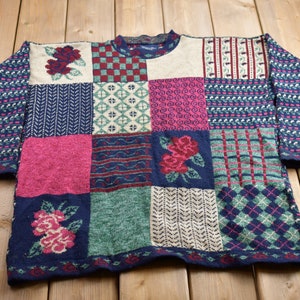 Könnte beinhalten: Ein Patchwork-Pullover mit verschiedenen Mustern und Farben, darunter Rot, Blau, Grün und Weiß. Der Pullover zeigt Blumenmuster und geometrische Muster.