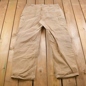 Puede incluir: Un pantal&oacute;n de trabajo de color beige con un parche de cuero marr&oacute;n en el bolsillo trasero derecho.