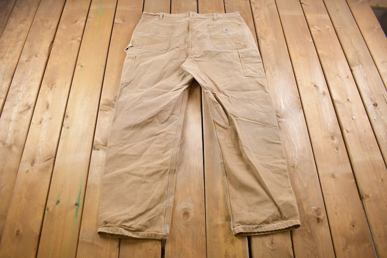 Puede incluir: Un pantal&oacute;n de trabajo de color beige con un parche de cuero marr&oacute;n en el bolsillo trasero derecho.