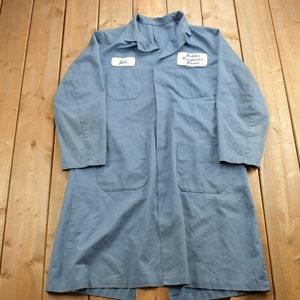 May include: A blue work coat with two white name tags. The top tag says "John" and the bottom tag says "Public Computer Room".