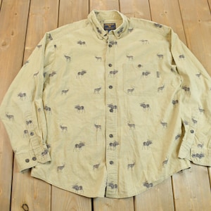 Puede incluir: Una camisa de manga larga de color beige con botones y un patrón repetido de siluetas de alces marrones.