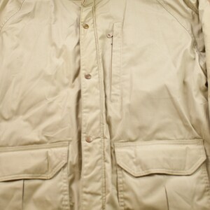 May include: A beige jacket with a button-up front, two large flap pockets, and a zippered pocket on the left side.