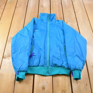May include: A blue and teal vintage jacket with a zipper closure. The jacket has a high collar and two pockets on the front.