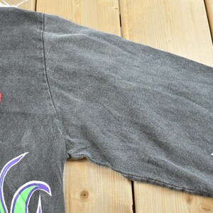 May include: Dark gray long-sleeve shirt with the word "ANGER" in red and gray, and "UCK" in green. The sleeves have a flame design in purple and green. The shirt is made of a soft, comfortable material.