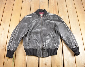 May include: A black leather bomber jacket with a ribbed knit collar, cuffs, and waistband. The jacket has a zipper closure and white piping along the seams.