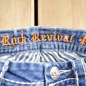 K&ouml;nnte beinhalten: Blaue Jeans aus Denim mit einem braunen gestickten Etikett mit der Aufschrift "Rock Revival" und einem Gr&ouml;&szlig;enetikett mit der Aufschrift "24".