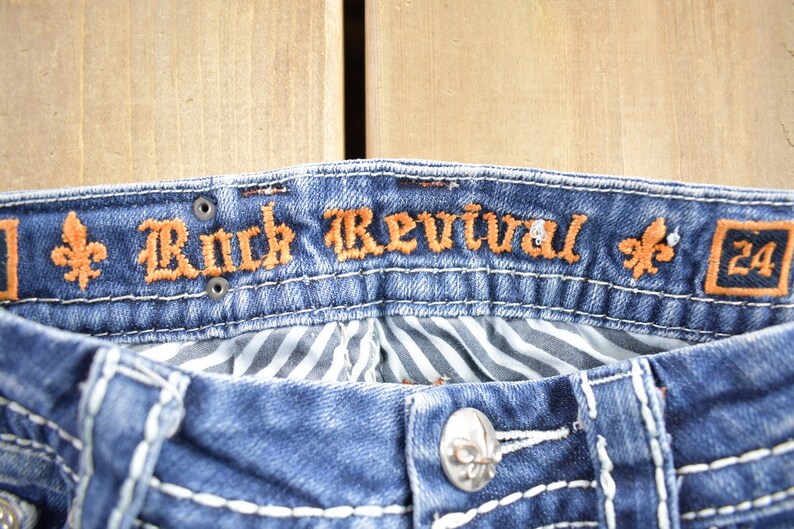 K&ouml;nnte beinhalten: Blaue Jeans aus Denim mit einem braunen gestickten Etikett mit der Aufschrift "Rock Revival" und einem Gr&ouml;&szlig;enetikett mit der Aufschrift "24".