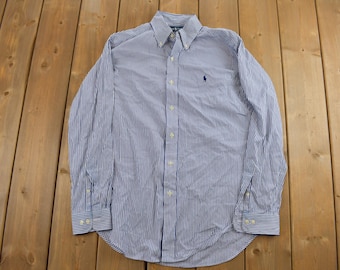 May include: A blue and white striped long-sleeve button-down shirt with a small polo player logo on the left chest.