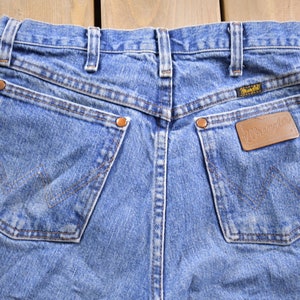 May include: A pair of blue denim jeans with a brown leather patch that says "Wrangler" on the back right pocket.