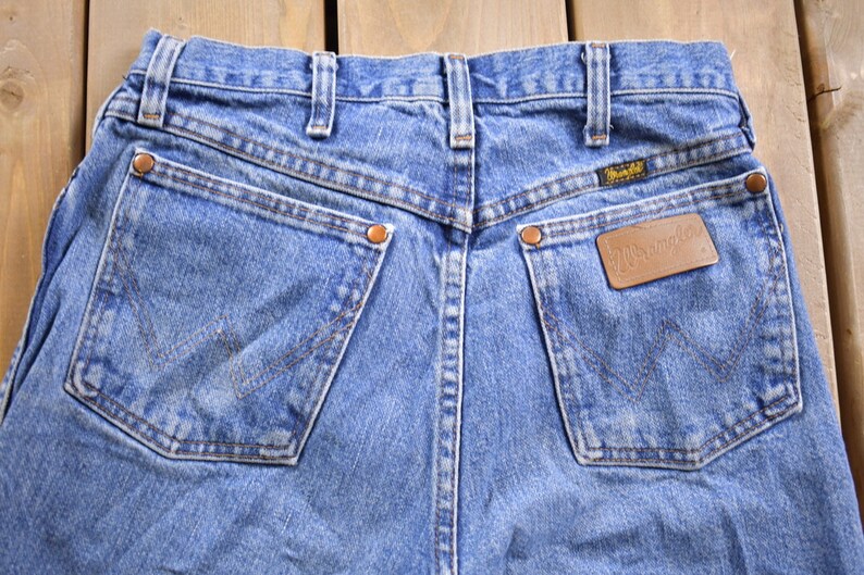 May include: A pair of blue denim jeans with a brown leather patch that says "Wrangler" on the back right pocket.