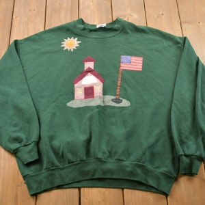 May include: Green sweatshirt with a red, white and blue schoolhouse, sun and American flag applique.