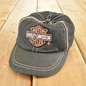 Peut inclure: Casquette de baseball noire avec le logo Harley-Davidson Cycles orange et blanc. La casquette a une visière incurvée et des coutures blanches. Le logo est centré à l'avant.