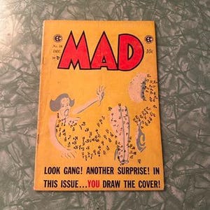 Puede incluir: Una portada de revista amarilla con la palabra "MAD" en letras rojas grandes. La portada presenta un dibujo animado de una mujer con una expresión de sorpresa. El texto debajo de la imagen dice "LOOK GANG! ANOTHER SURPRISE! IN THIS ISSUE...YOU DRAW THE COVER!"
