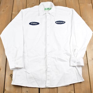 May include: White long-sleeve button-up shirt with two blue oval patches. The left patch says "J. White" and the right patch says "NetJets".