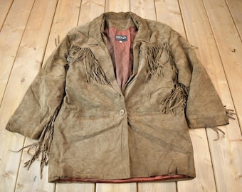 May include: A brown suede jacket with fringe detailing. The jacket has a button closure and a label that reads "Sierra".