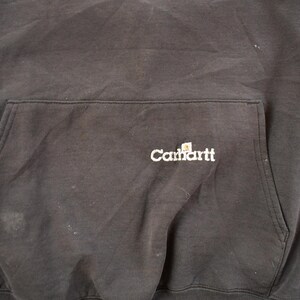 May include: Dark gray Carhartt hoodie with a front pocket. The Carhartt logo is embroidered in white on the pocket. The fabric appears worn and slightly faded.