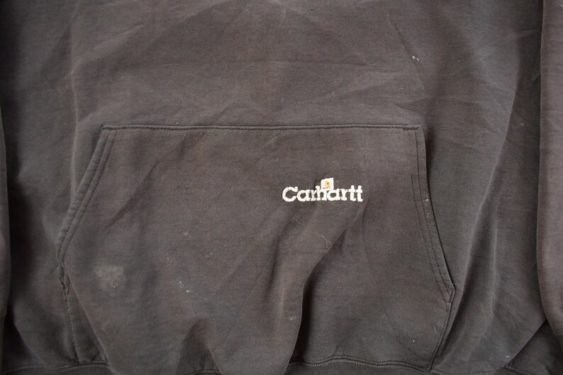 May include: Dark gray Carhartt hoodie with a front pocket. The Carhartt logo is embroidered in white on the pocket. The fabric appears worn and slightly faded.