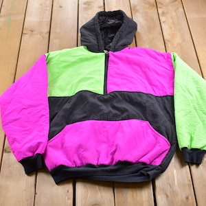 May include: A black, pink, and green hooded jacket with a zipper closure. The jacket has a large pocket on the front.