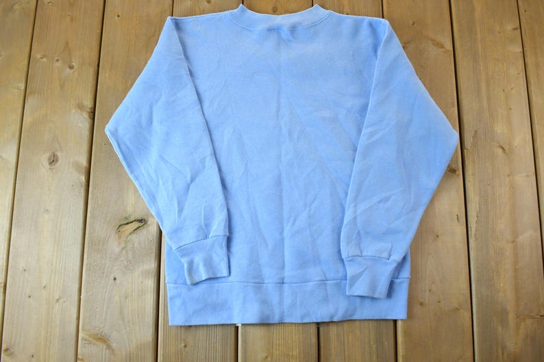 May include: A light blue sweatshirt with long sleeves and a crew neck.