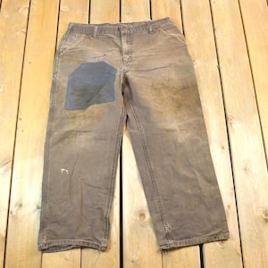 May include: A pair of brown work trousers with a dark blue patch on the right knee. The trousers are worn and have a faded appearance.