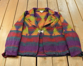 May include: A long-sleeve blazer featuring a vibrant, multi-colored geometric pattern in shades of purple, orange, red, green, and yellow. The jacket has a notched lapel, long sleeves, and is secured at the front with a circular silver-toned metal clasp.