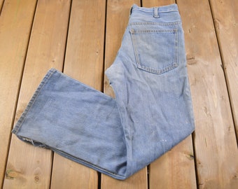 Può includere: Un paio di jeans in denim blu chiaro piegati a metà su una superficie di legno.