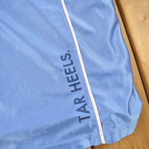 May include: Light blue athletic shorts with a white stripe down the side and the text "TAR HEELS" embroidered in navy blue.