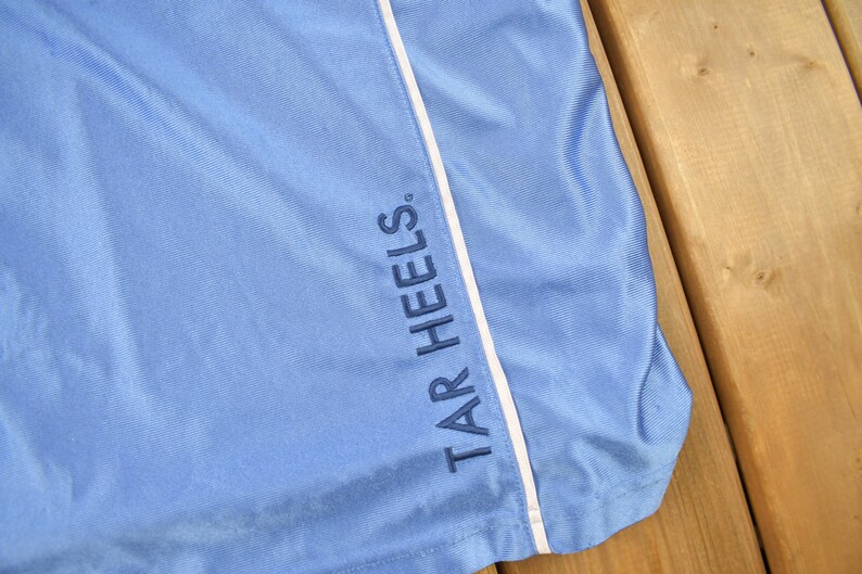 May include: Light blue athletic shorts with a white stripe down the side and the text "TAR HEELS" embroidered in navy blue.