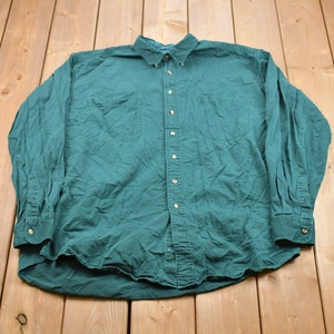 May include: A long-sleeved, button-down shirt in a deep green color. The shirt has a classic fit and two chest pockets.