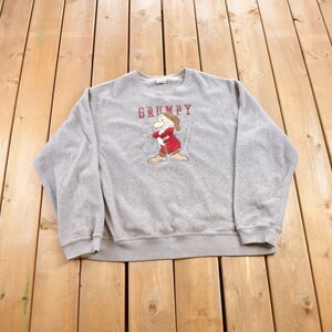 May include: A grey sweatshirt featuring a cartoon image of Grumpy from Snow White and the Seven Dwarfs. The text "GRUMPY" is printed above the image.