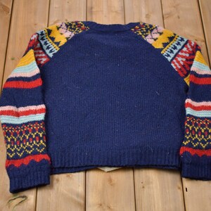 May include: A navy blue sweater with colorful geometric patterns on the sleeves. The sweater has a crew neck and long sleeves.