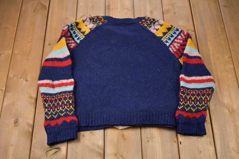 May include: A navy blue sweater with colorful geometric patterns on the sleeves. The sweater has a crew neck and long sleeves.