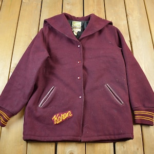 May include: A maroon wool varsity jacket with a large "Karon" patch on the front. The jacket has a hood, two pockets, and a button closure.
