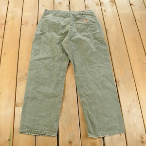 Puede incluir: Vista trasera de pantalones de trabajo verde oliva con m&uacute;ltiples bolsillos y un peque&ntilde;o logotipo. Los pantalones est&aacute;n hechos de una tela duradera y tienen un ajuste relajado, adecuados para diversas tareas.