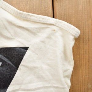 May include: Close-up of a white t-shirt with a black and white geometric design. The shirt has a seam along the shoulder and a small stain.
