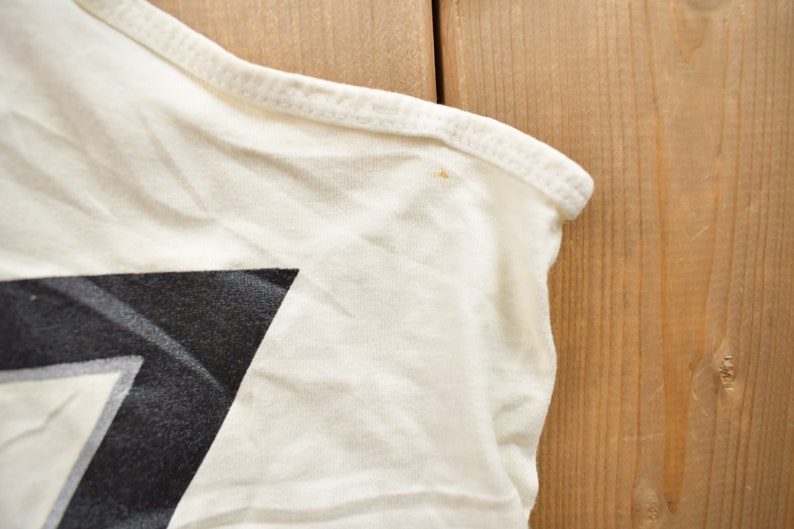 May include: Close-up of a white t-shirt with a black and white geometric design. The shirt has a seam along the shoulder and a small stain.