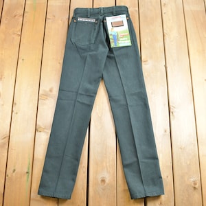 Op de afbeelding: Een donkergroene jeans met een bruine leren patch op de achterzak. De jeans heeft een rechte pijp en een klassieke pasvorm. De jeans ligt plat op een houten oppervlak.