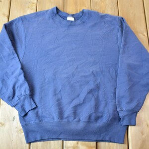 Könnte beinhalten: Ein einfarbiger, blauer, langarmiger Pullover mit Rundhalsausschnitt.