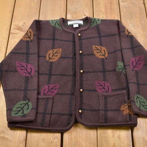 May include: A brown cardigan sweater with a plaid pattern and leaf designs. The cardigan has a button closure and two pockets.