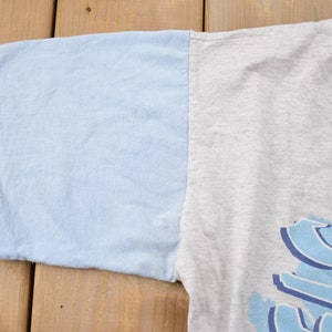 May include: A gray and light blue t-shirt with a blue graphic print of the word "SURF".