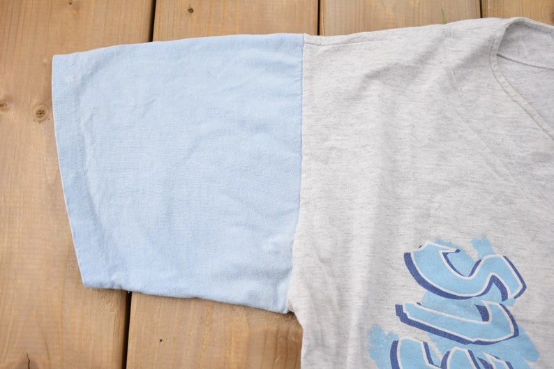 May include: A gray and light blue t-shirt with a blue graphic print of the word "SURF".