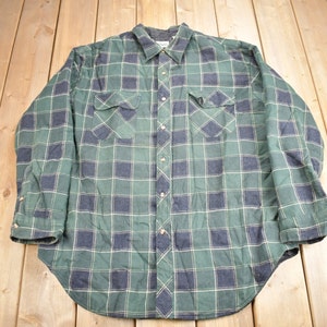 Puede incluir: Una camisa de franela a cuadros verde y negro con mangas largas y cierre de botones.