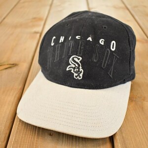 Könnte beinhalten: Schwarze Baseballkappe mit gebogenem Schirm. Auf der Kappe steht in weißer Schrift "CHICAGO WHITE SOX", mit dem Logo des Teams auf der Vorderseite. Der Schirm ist hellbeige.