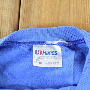 Puede incluir: Una sudadera azul Hanes con una etiqueta que dice "30% Algod&oacute;n/Coton 50% Acr&iacute;lico/Acrylique" y "XL 46-48" y "Hecho en EE. UU. Fabrique aux E.U."