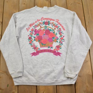May include: A grey sweatshirt with a floral design and the text "La Rue a la Campagne Francaise" printed on the front.