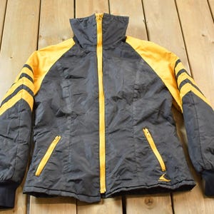 May include: A black and yellow jacket with a zipper closure and a high collar. The jacket has yellow stripes on the sleeves and a yellow zipper.