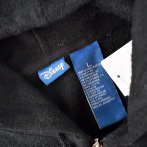 May include: A black hooded sweatshirt with a blue Disney label and a blue care label. The care label lists the fabric as 100% polyester.